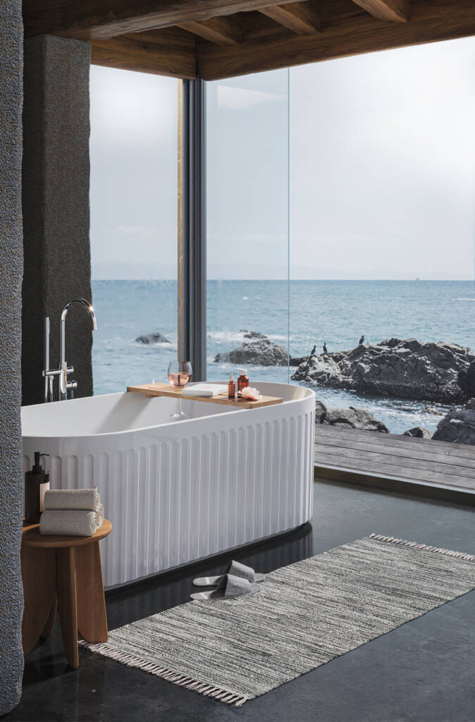 A minimalist freestanding bathtub with a tap, set in a serene room overlooking the ocean, bathed in natural light.